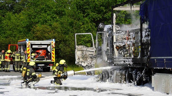 Feuerwehrleute löschen einen brennenden Lkw.