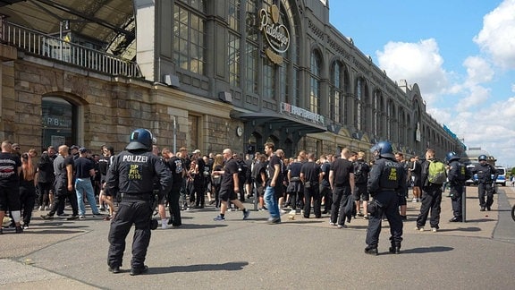 Behelmte Polizisten stehen vor einem Bahnhof. Die Beamten beobachten mehrere rechte Demonstranten