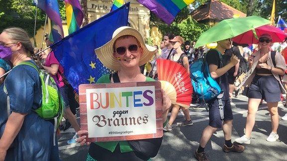 Eine Frau hält ein Schild in die Kamera auf dem steht: bunt statt braun