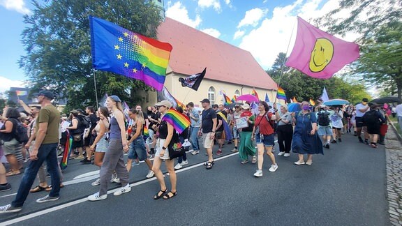 Menschen mit bunten Flaggen und der Regenbogenfahne laufen auf einer Straße  