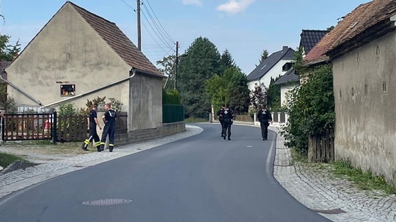 Männer in dunkler Kleidung laufen durch ein Dorf. 