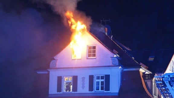 Aus dem Dachgeschoss eines Hauses lodern Flammen.