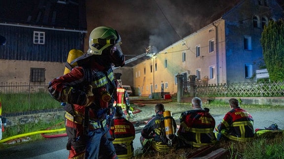 Mehrere Feuerwehrleute vor einem brennenden Haus