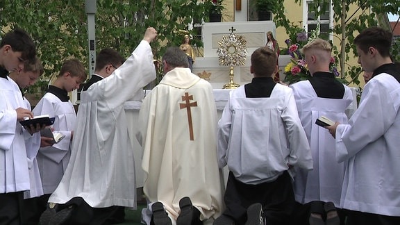 Ein katholischer Pfarrer und mehrere Messdiener knien in Ralbitz vor einem Altar unter freiem Himmel