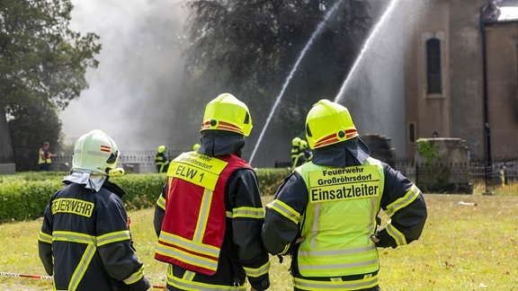 Qualm steigt aus der Stadtkirche Großröhrsdorf empor, während Feuerwehreinsatzkräfte löschen.