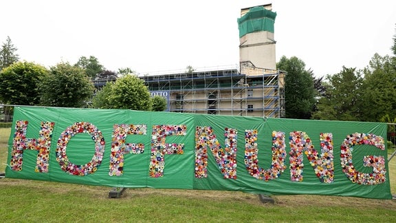 Zahlreiche gehäkelte Blüten auf einem Plakat bilden das Wort „Hoffnung“ auf dem Friedhof vor der beschädigten Stadtkirche Großröhrsdorf.