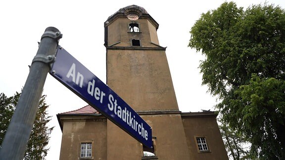 Blick auf das Straßenschild "An der Stadtkirche" vor der beschädigten Turmspitze