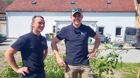 Ein Maibaum wird aufgestellt: Zwei Männer lachen in die Kamera