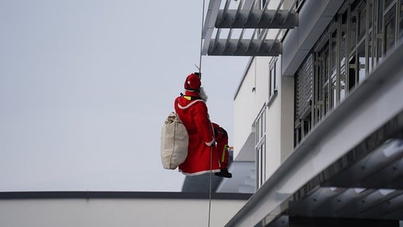 Ein Feuerwehrmann der Höhenrettung seilt sich im Nikolauskostüm an einer Kinderklinik ab.
