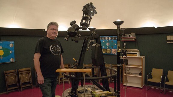 Ein Mann steht neben dem Projektor im Planetarium Hoyerswerda und schaut zur Kamera. 