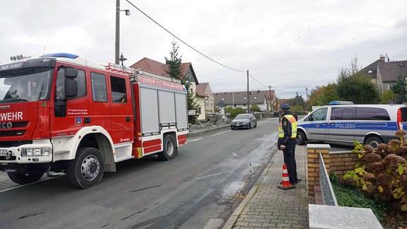 Ein Polizist steht in einer Straße neben einem Feuerwehrauto. 