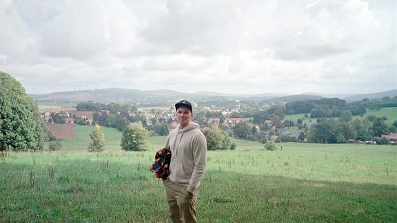 Ein Junger Mann steht vor einer Landschaft unter wolkigem Himmel