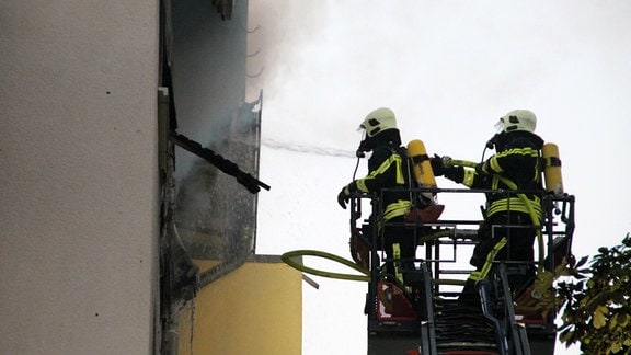 Feuerwehrleute stehen auf der Drehleiter und löschen eine brennende Wohnung im vierten Stock.