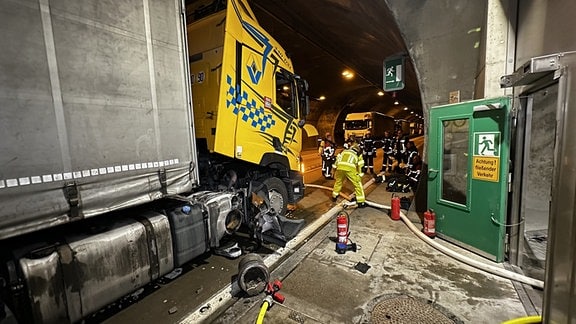 Ein Lkw steht in einem Tunnel und wird von Feuerwehr und Monteuren begutachtet. Erkennbar hatte der Laster ein Problem.