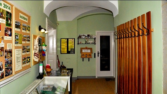 Blick in einen Ausstellungsraum im Karasek-Museum: auf der linken Seite eine Vitrine, darüber Tafeln, rechts eine hölzerne Garderobe. 