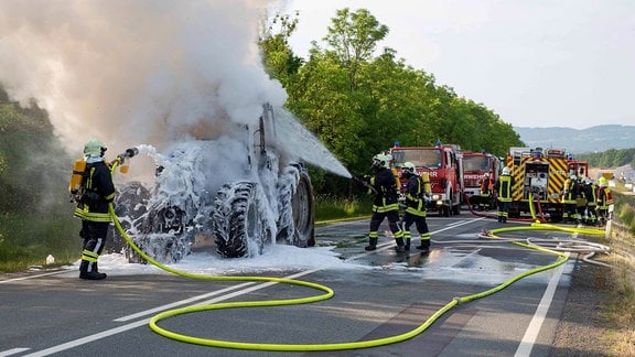 Feuerwehrleute löschen einen brennenden Traktor