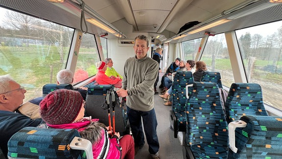 In einem Zug der Trilex-Linie 9 sitzen Fahrgäste. Zwischen ihnen steht der Zittauer Stadtrat und Wanderführer Matthias Böhm.