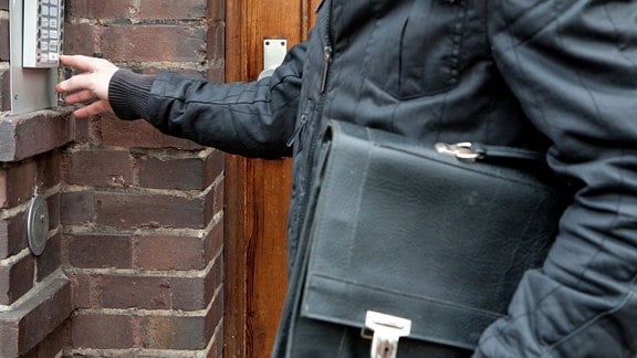 Eine Person mit Aktentasche klingelt an einer Tür.