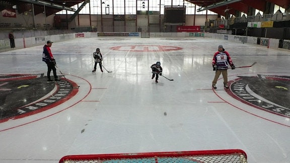 Erwachsene und Kinder spielen Eishockey in der Halle.