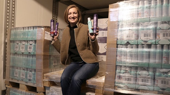 Jana Groß, Produktmanagerin bei Fit, sitzt auf angelieferten Paletten und hält Spraydosen in den Händen.