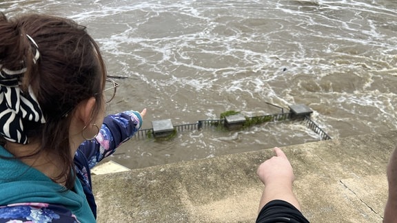 Eine Frau und ein Mann zeigen auf eine von Hochwasser betroffene Stelle an der Neiße in Görlitz. 