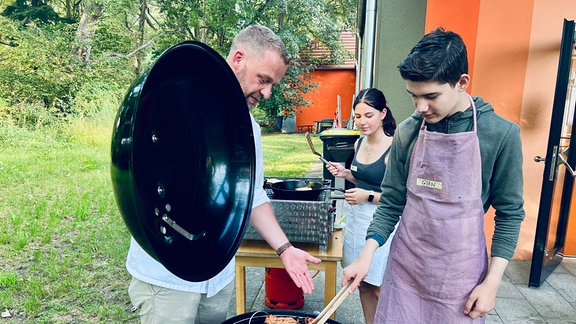 Mann grillt zusammen mit zwei Jugendlichen