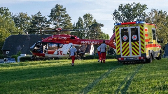 Ein Hubschrauber und ein Rettungswagen stehen auf einer Wiese. 