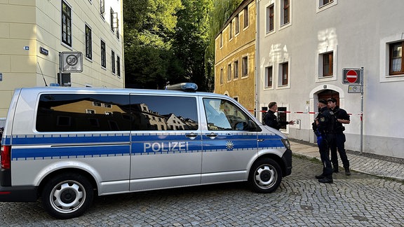 Polizeiauto und Polizisten stehen vor einem Gebäude