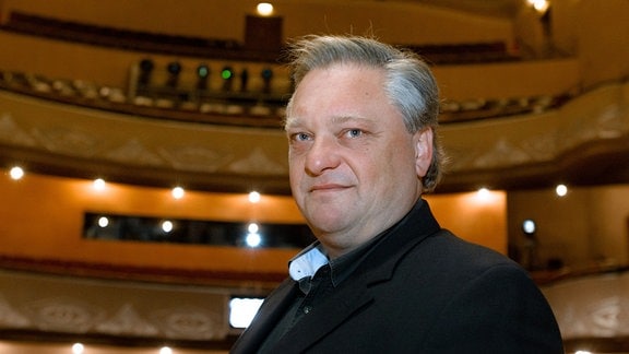 Roman Brogli-Sacher, ein Mann mit grauen Haaren in schwarzem Anzug steht in einem Theater