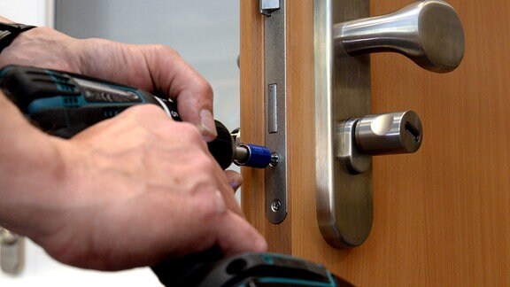 Ein Mitarbeiter eines Schluesseldienstes montiert zur zusätzlichen Sicherung gegen Einbruch einen elektronischen Schliesszylinder an einer Tür.