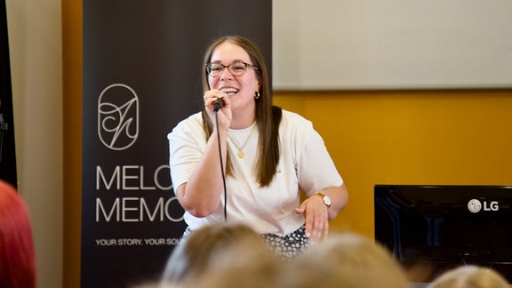 Eine Frau singt lachend in ein Mikrofon.