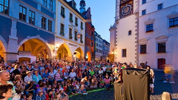 In der Görlitzer Innenstadt haben sich in der Abenddämmerung zahlreiche Menschen versammelt, um einer Theatervorstellung zu zusehen.