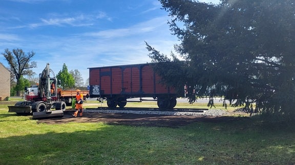 Ein Baugerät steht neben einem roten Waggon.