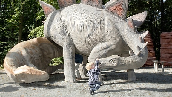 Allosaurus (links) und Stegosaurus (rechts) mit Kind am Maul.