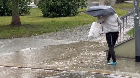 Person mit Regenschirm wadet durch überfluteten Weg