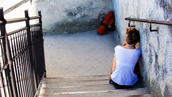 Angelehnt an die Wand sitzt eine junge Frau auf einer Treppe