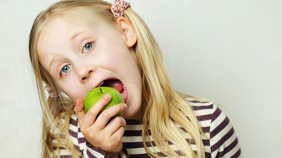 Kind isst einen grünen Apfel.