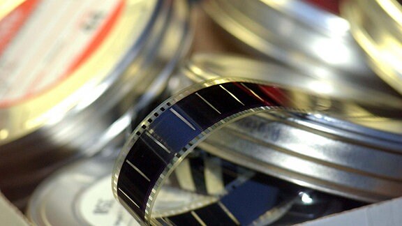 Eine Kinofilmrolle hängt aus einer Filmdose heraus.