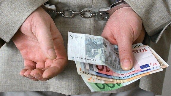 Ein Mann in Handschellen hält Geldscheine in einer Hand