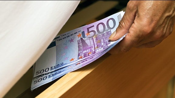 Ein Mensch versteckt mehrere 500 Euro Scheine unter einer Matratze.