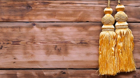 Goldenes Seil mit Quaste (Posamenten) vor einer Holzwand