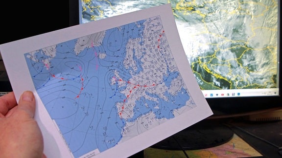 Eine Person informiert sich auf dem Ausdruck einer Bodenanalysekarte des Deutschen Wetterdienstes und einem Satellitenbild auf dem Monitor eines Computers über ein bevorstehendes Unwetterereignis Nordrhein-Westfalen