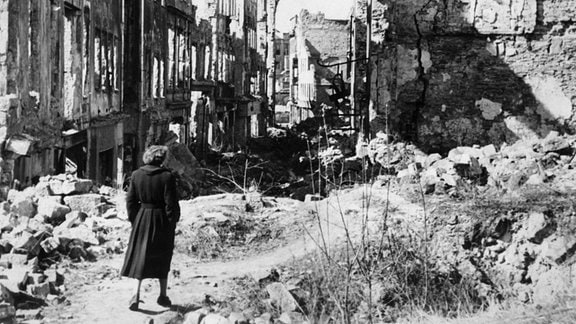 Eine Frau geht in einer Straße in Dresden an Häusern vorbei, von denen nach Bombenangriffen im Zweiten Weltkrieg nur noch Ruinen geblieben sind. 
