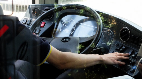 Die Fahrerkabine eines Busses der LVB. Zu sehen ist das Lenkrad und der Busfahrer von der Seite, wie er einen Knopf drückt.