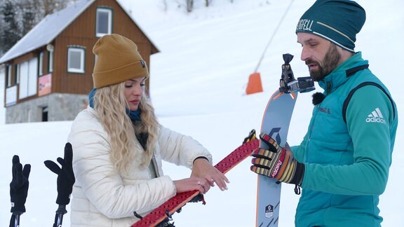 Eine Frau und ein Mann bringen Steigfelle an einem Ski an. 