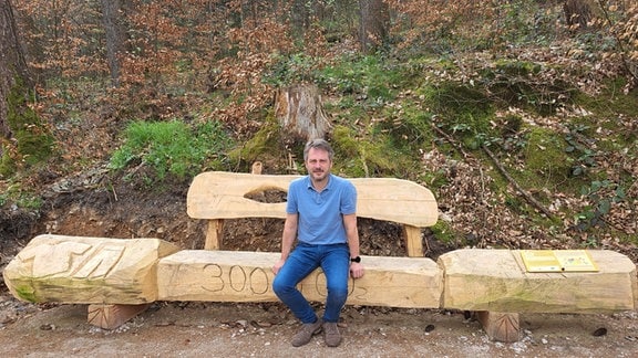 Ein Mann sitzt auf einer Holzbank. 