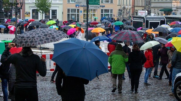 Auf dem Marktplatz von Annaberg-Buchholz stehen Menschen mit Regenschirmen in der Hand