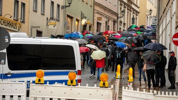 Menschen mit Regenschirmen laufen in Annaberg-Buchholz eine Straße entlang. Im Vordergrund steht ein Polizeifahrzeug