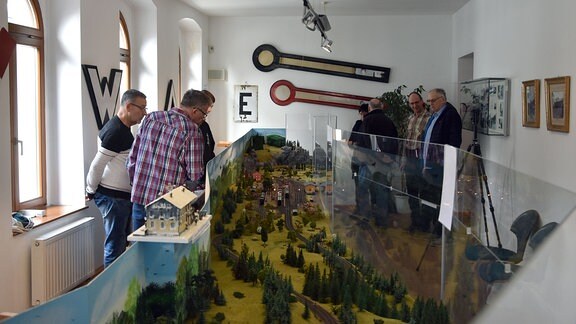 Blick in einen Ausstellungsraum mit langgezogener Modellbahnanlage und Besuchern.