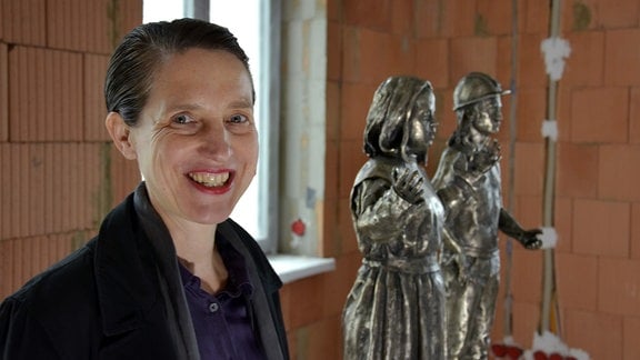 Die Künstlerin Christina Doll vor ihren Skulpturen, einem Engel und einem Bergmann.